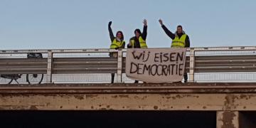Three Dutch yellow vests holding up a sign demanding democracy
