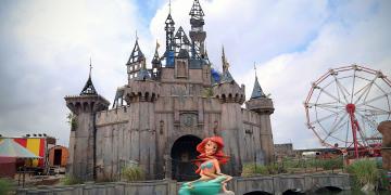 Dismaland distorted mermaid ariel and a broken down castle in the background 